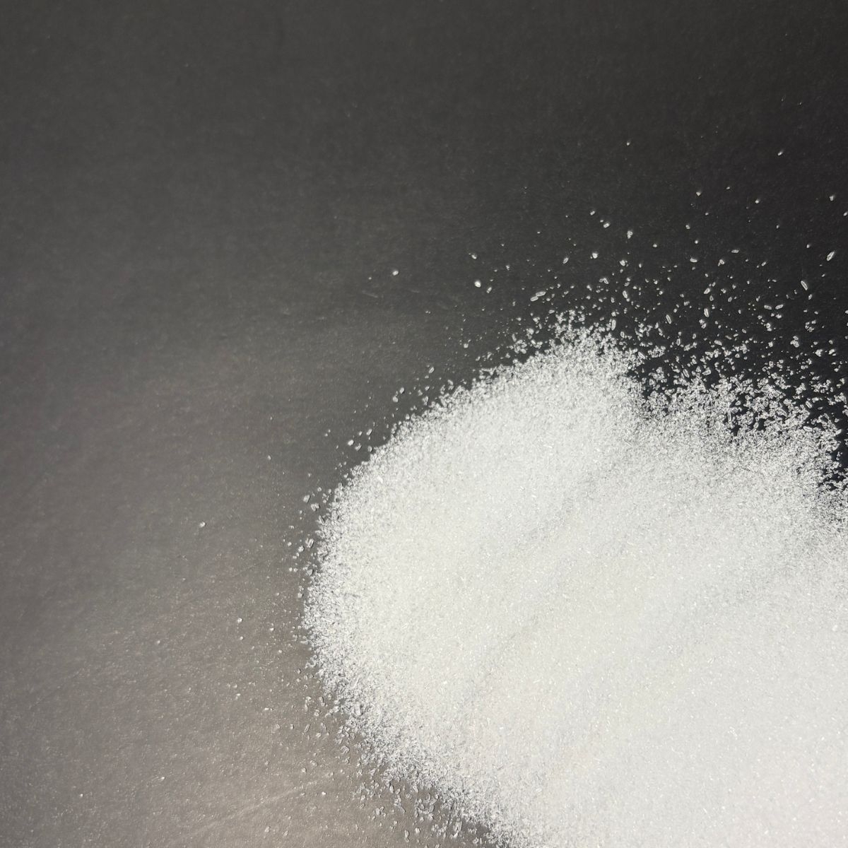 weisses Natriumcitrat-Granulat auf dunklem Untergrund verteilt