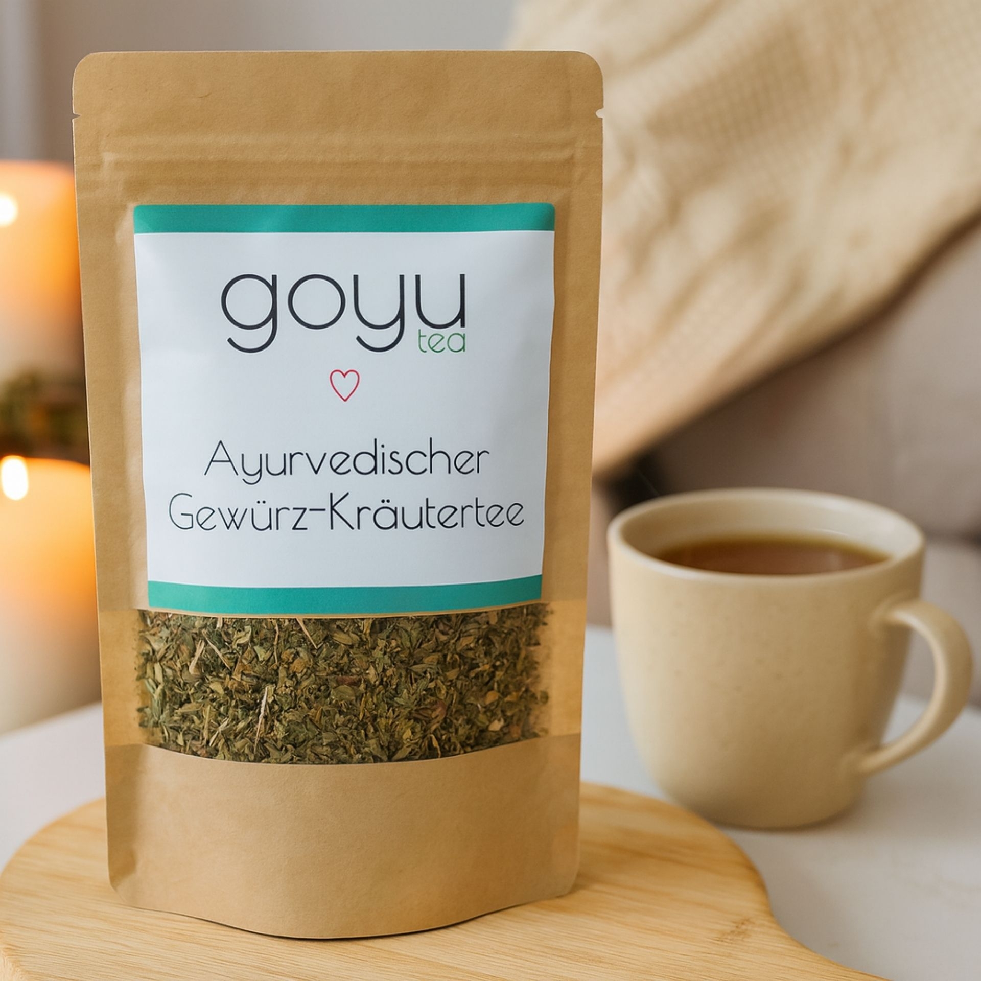 Beutel „Ayurvedischer Gewuerz-Kraeutertee“ von goyu tea_ daneben eine helle Tasse Tee_ im Hintergrund Kerzen und Decke
