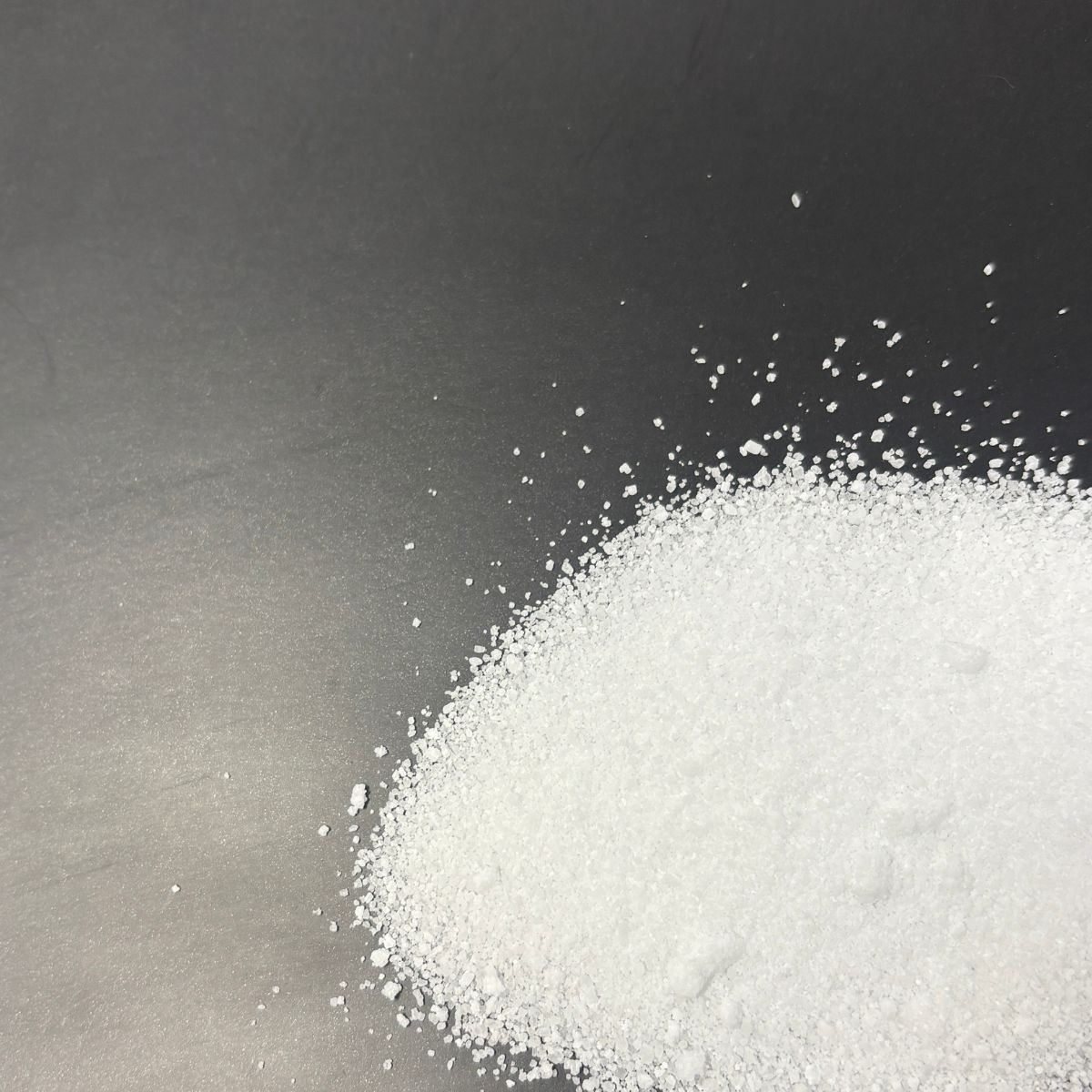 Weisse Calciumchlorid-Kristalle auf dunkler Oberflaeche verstreut