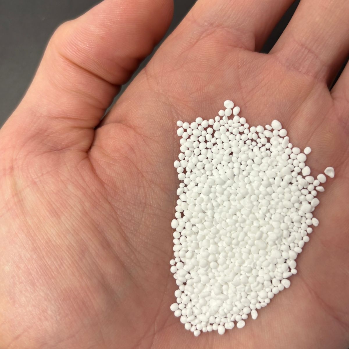 Kaliumcarbonat-Granulat in einer geoeffneten Hand dargestellt