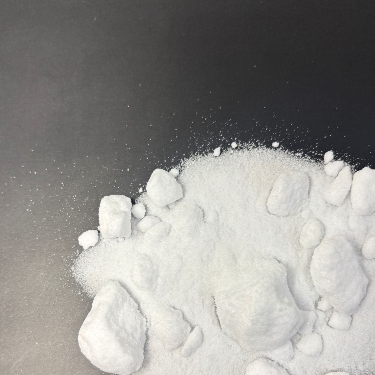 Weisses Kaliumchlorid-Pulver mit groben Stuecken auf schwarzem Untergrund
