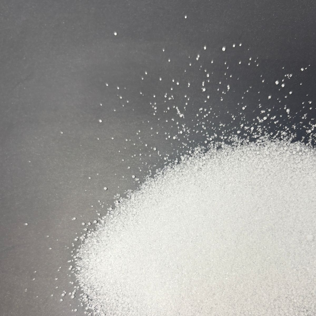 Feinkoerniges weisses Natriumchlorid auf grauem Untergrund verstreut