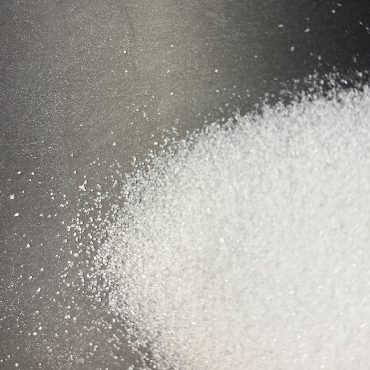 Feinkoernige weisse Ascorbinsaeure auf dunklem Untergrund verteilt