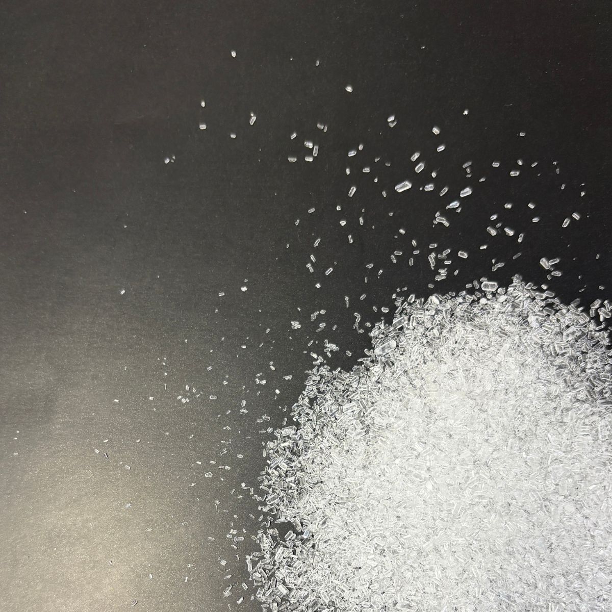 Klarglaenzende Magnesiumsulfatkristalle auf dunklem Untergrund verstreut