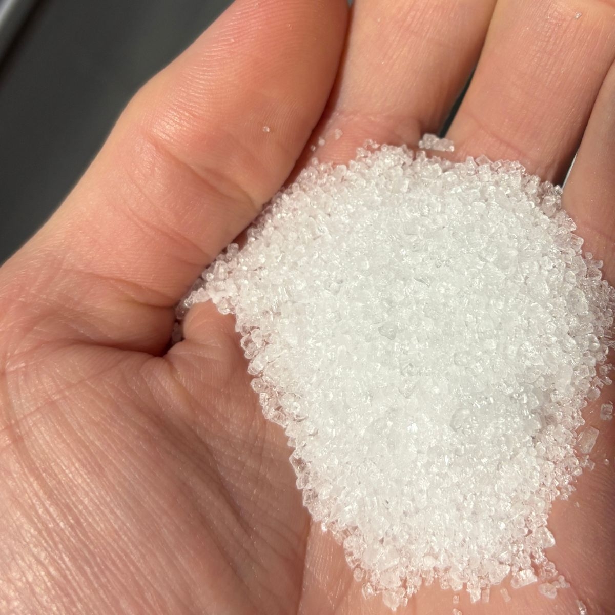 Natriumthiosulfat-Kristalle in einer Hand auf heller Hautfarbe