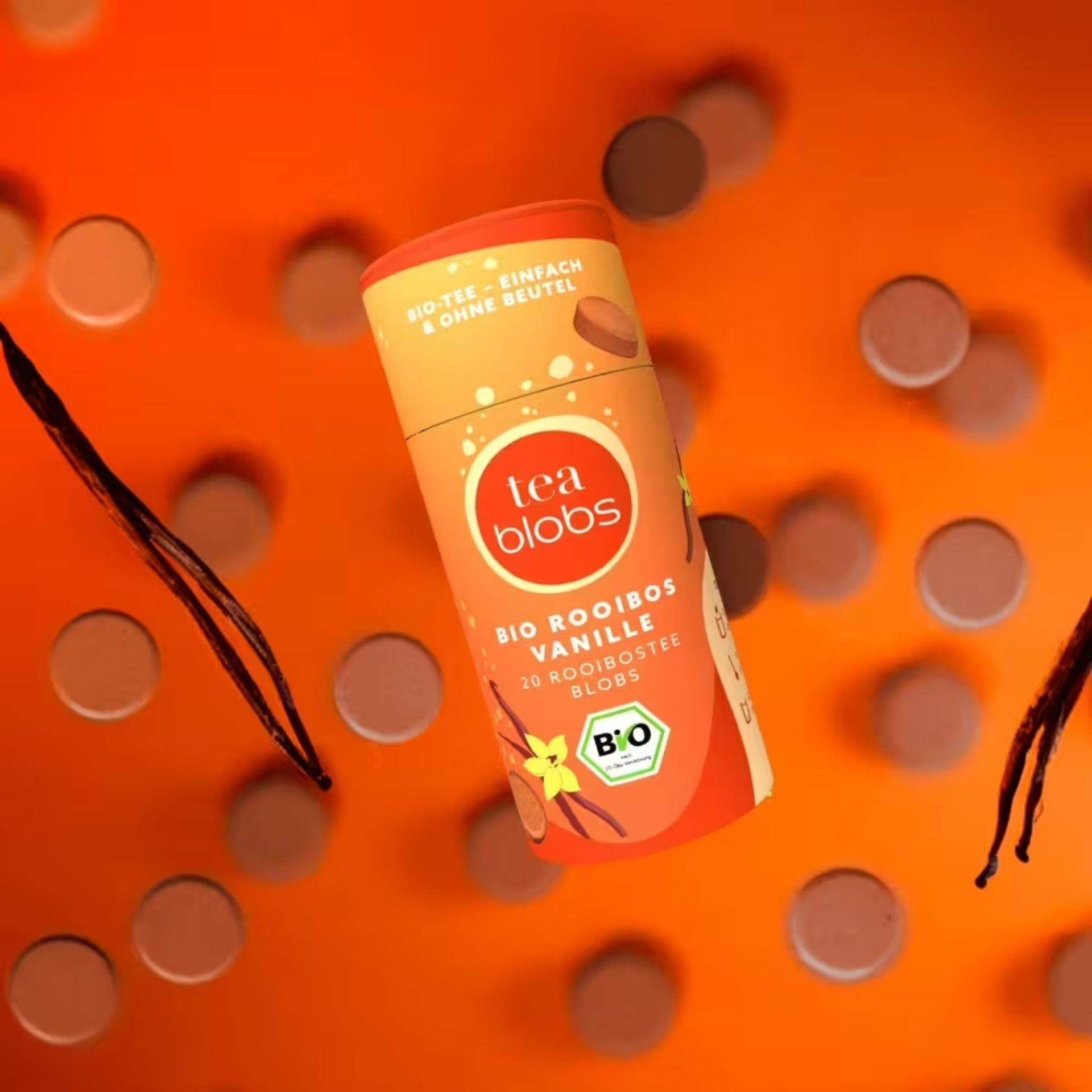 TeaBlobs BIO Rooibos Vanille Dose umgeben von Tee-Blobs und Vanilleschoten auf orangem Hintergrund