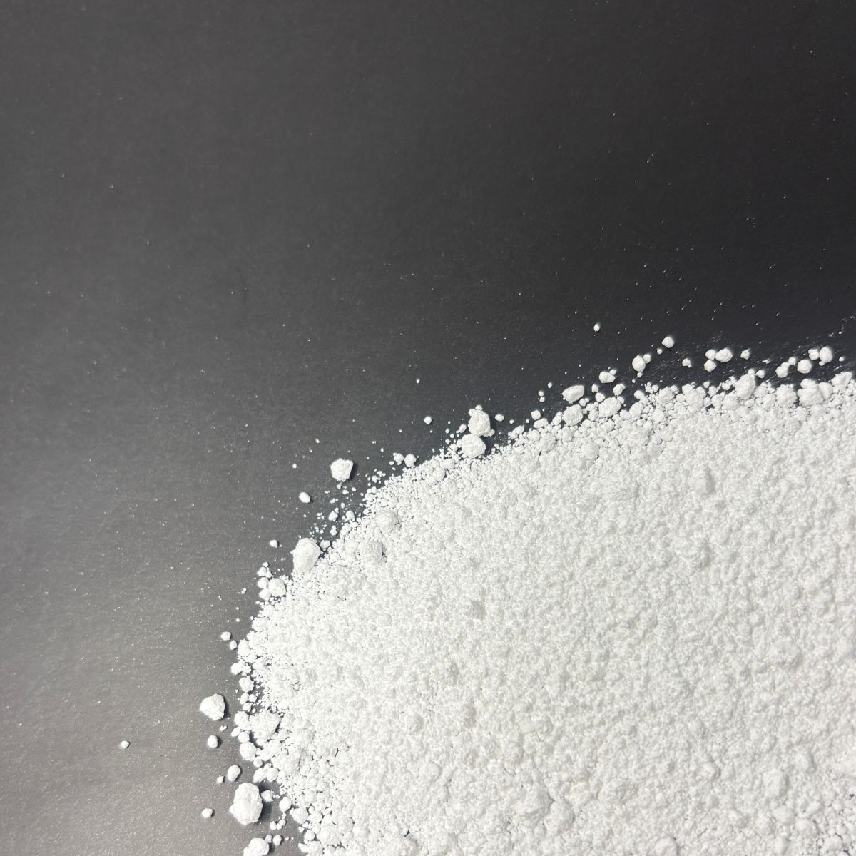 Magnesiumcarbonat als feines weisses Pulver auf dunklem Untergrund