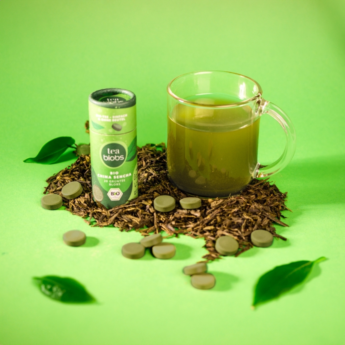 Bio China Sencha Teablobs neben Glas Tee auf losem Tee und gruenem Hintergrund