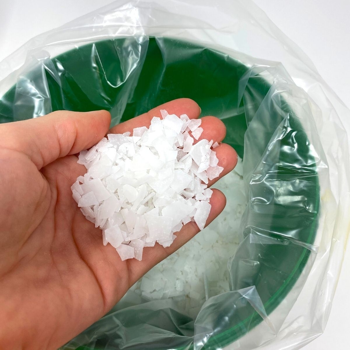 Hand haelt weisse Magnesiumflakes ueber geoeffnetem gruenen Eimer