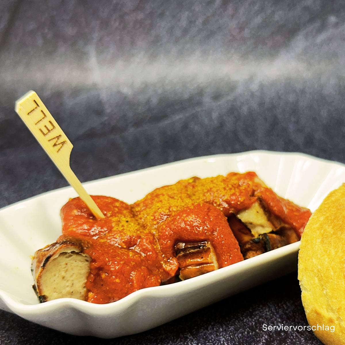 Currywurst in weisser Schale mit Sauce und Currypulver_ daneben ein Broetchen