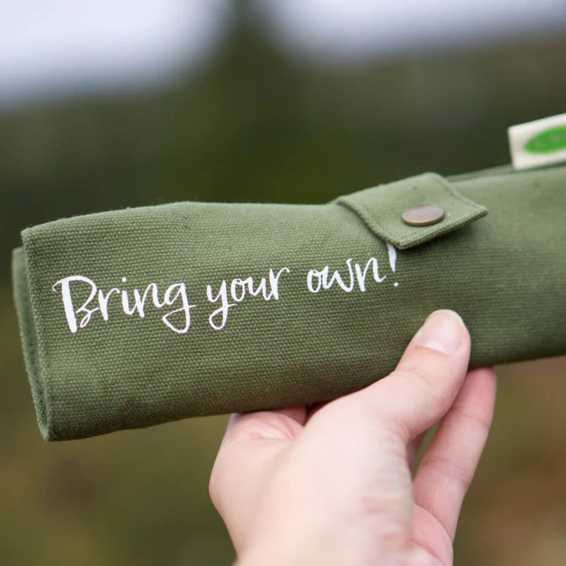 Zusammengerolltes gruenes Etui des Kokosnuss-Bestecksets mit Aufdruck „Bring your own!“