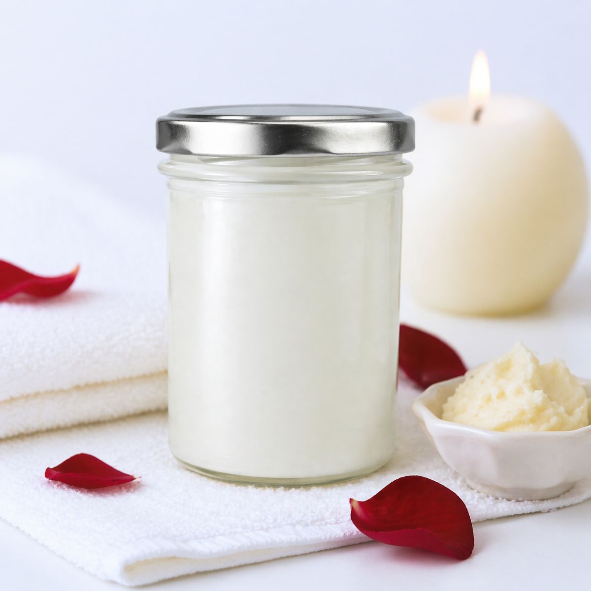 Glas mit 350ml reiner Bio Sheabutter auf Handtuch mit Kerze und Rosenblaettern