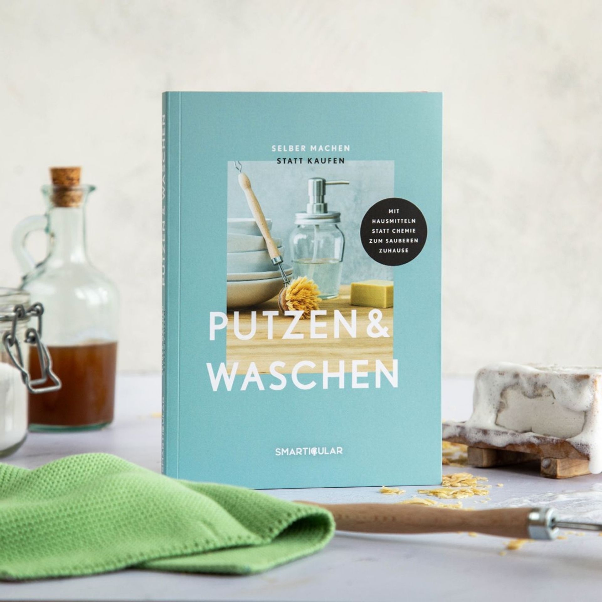 Selber machen statt kaufen – Putzen _ Waschen aufgestellt neben Seife_ Flaschen und gruenem Reinigungstuch