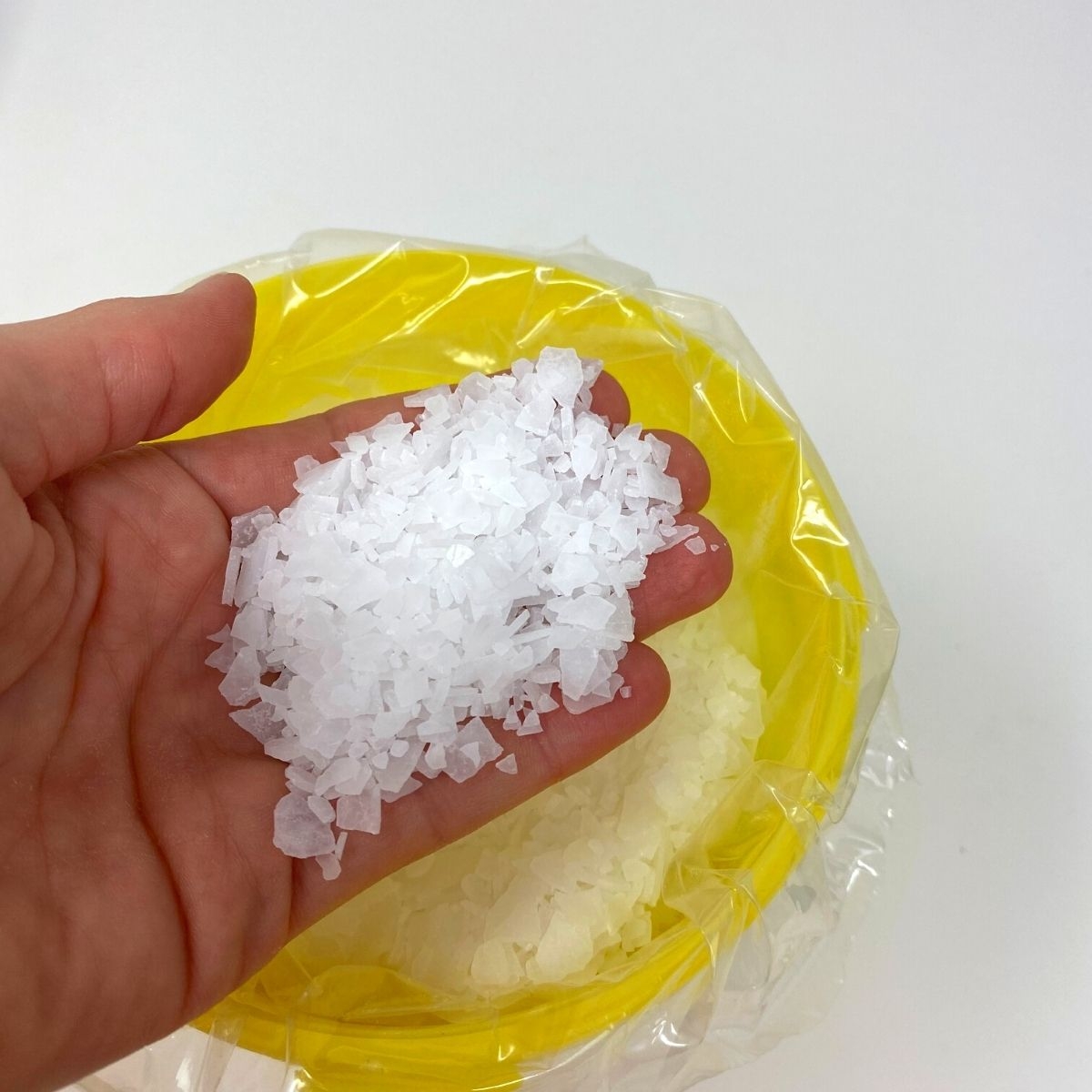 Hand haelt weisse Magnesium Flakes ueber geoeffnetem gelben Eimer