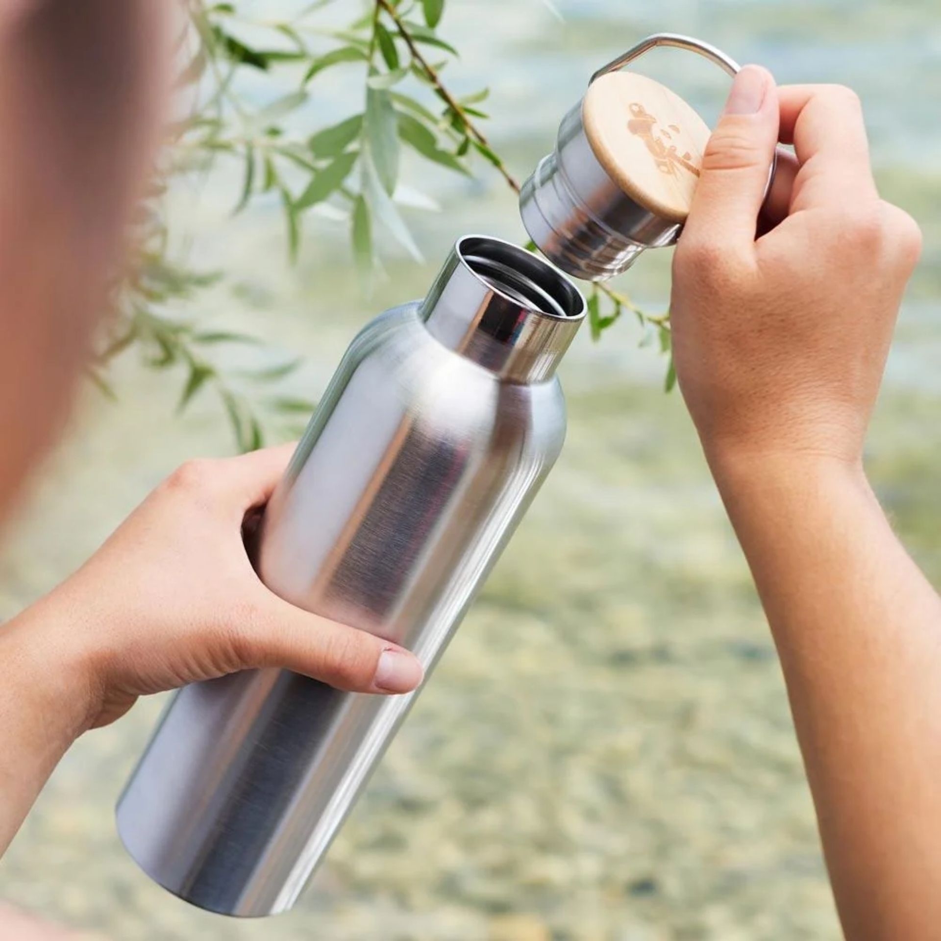 pandoo Edelstahl Trinkflasche 750 ml beim Oeffnen des Bambusdeckels im Freien