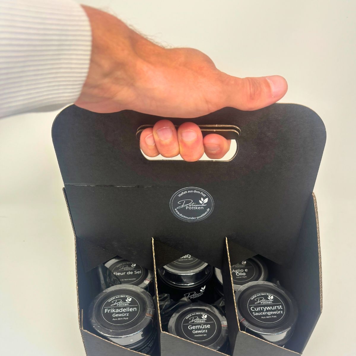 Hand haelt schwarze Box mit sechs Dortmunder Poettken Gewuerzglaesern
