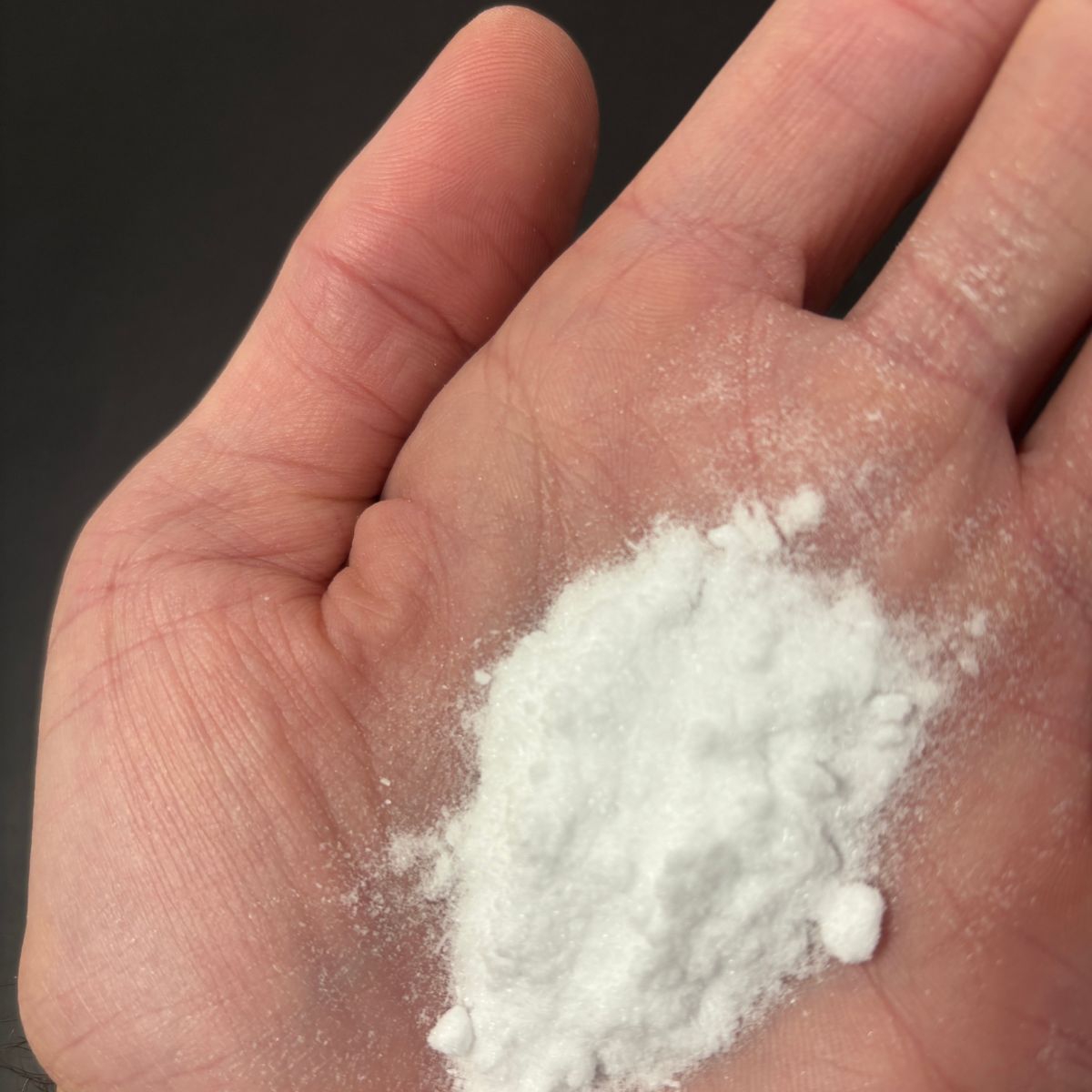 Hand haelt feines weisses Dextrose-Pulver ueber dunklem Hintergrund