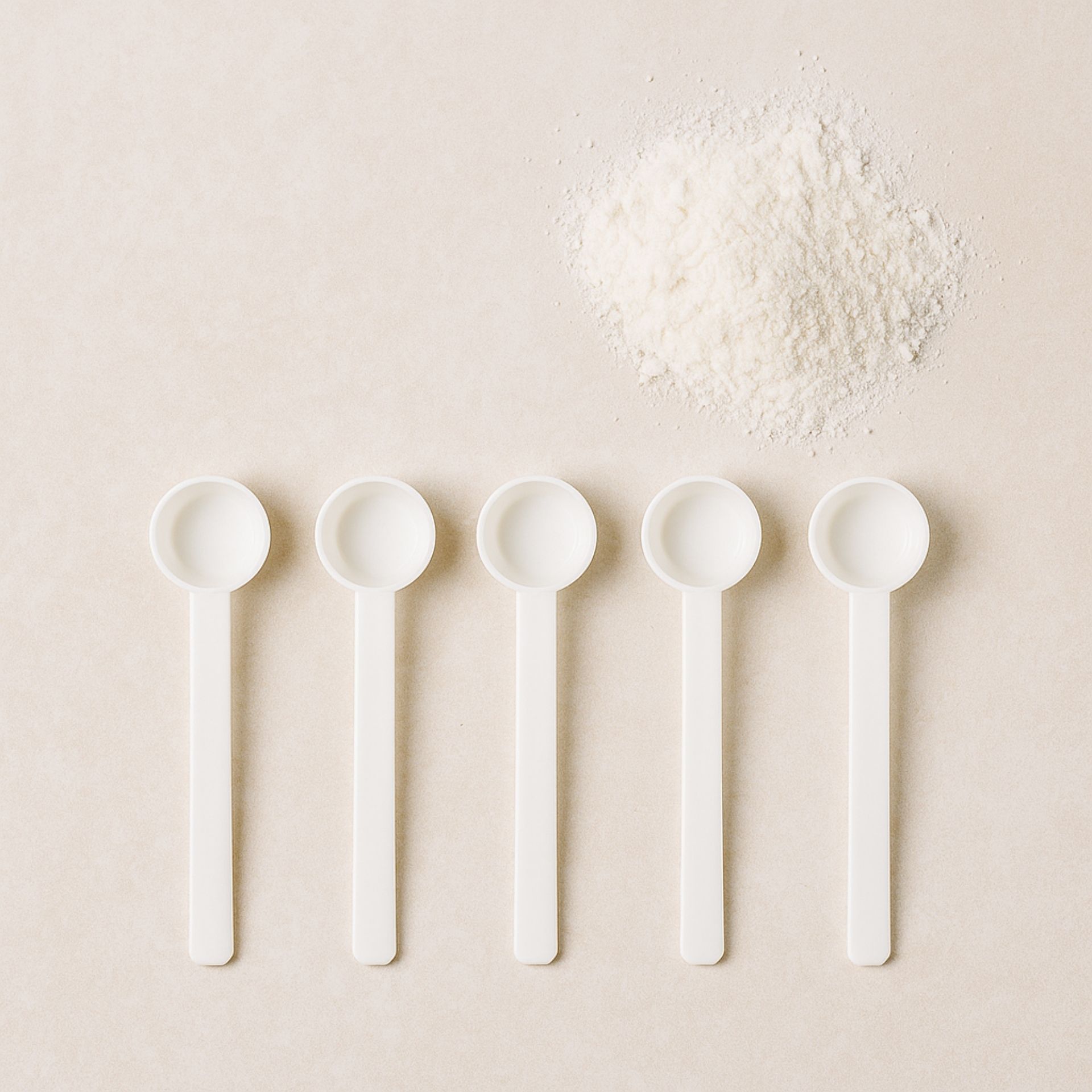 Fünf weiße 1-ml-Messlöffel in einer Reihe, daneben Pulver auf hellem Untergrund.