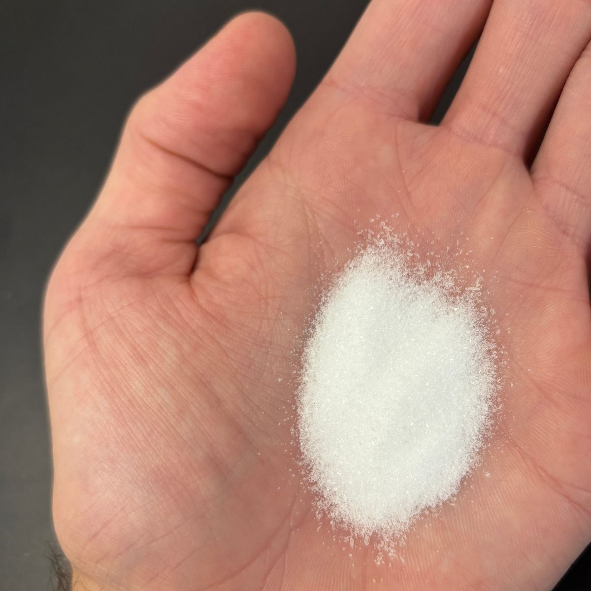 feinkoerniges weisses Natriumcitrat in einer Hand gehalten