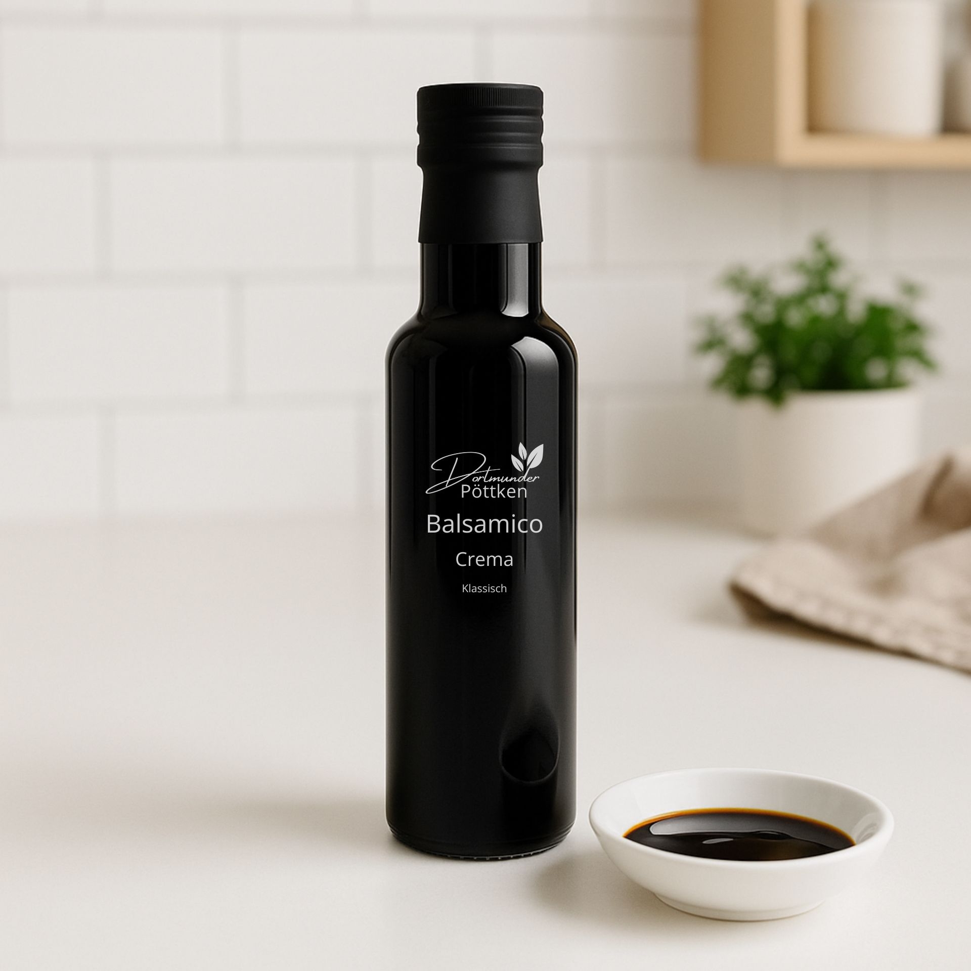 Flasche Balsamico Crema klassisch 250ml mit kleiner Schale Crema auf heller Kuechenoberflaeche und gruenem Deko-Element