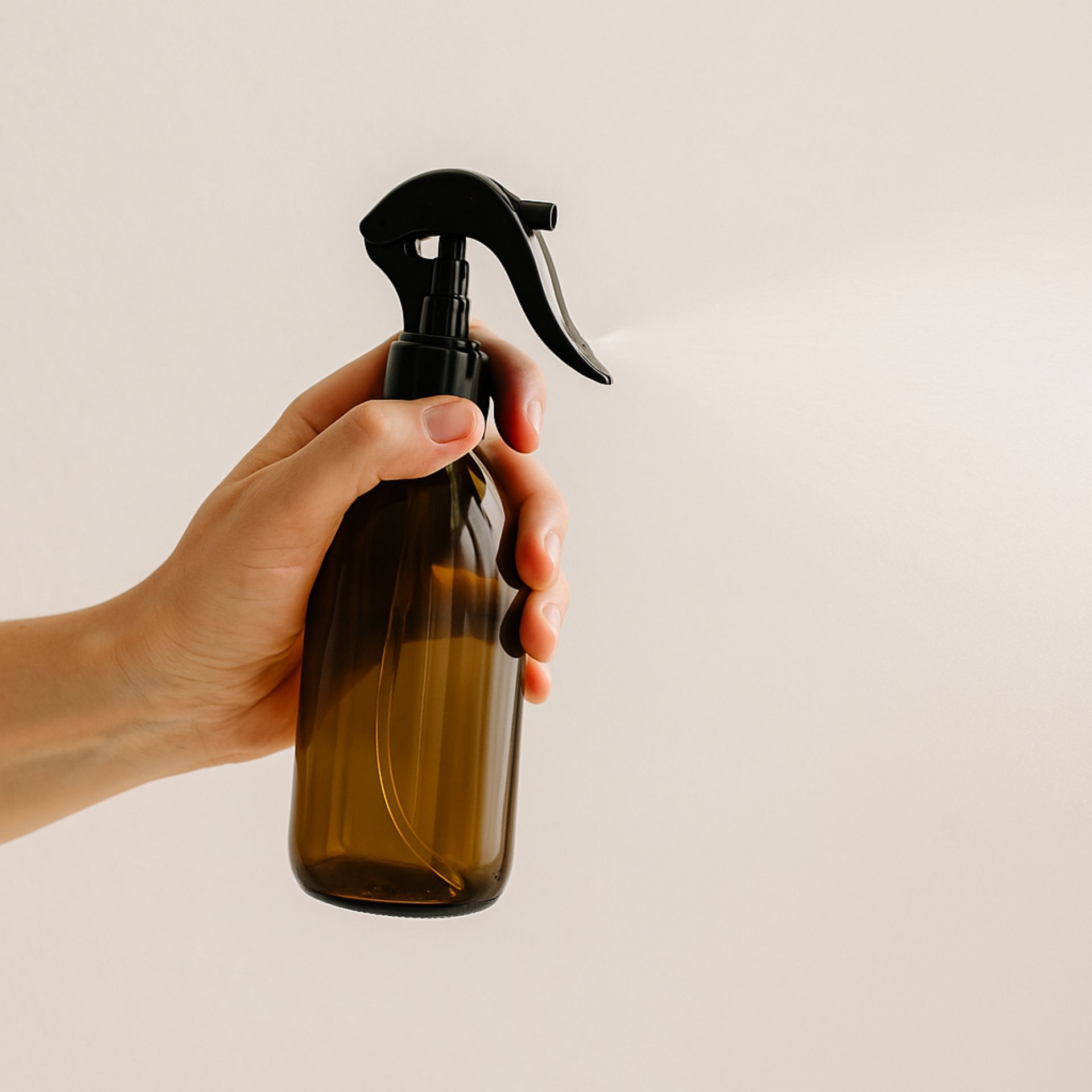 Hand haelt braune Glasflasche 250ml mit schwarzem Mini-Trigger-Spruehkopf_ feiner Spruehstrahl sichtbar