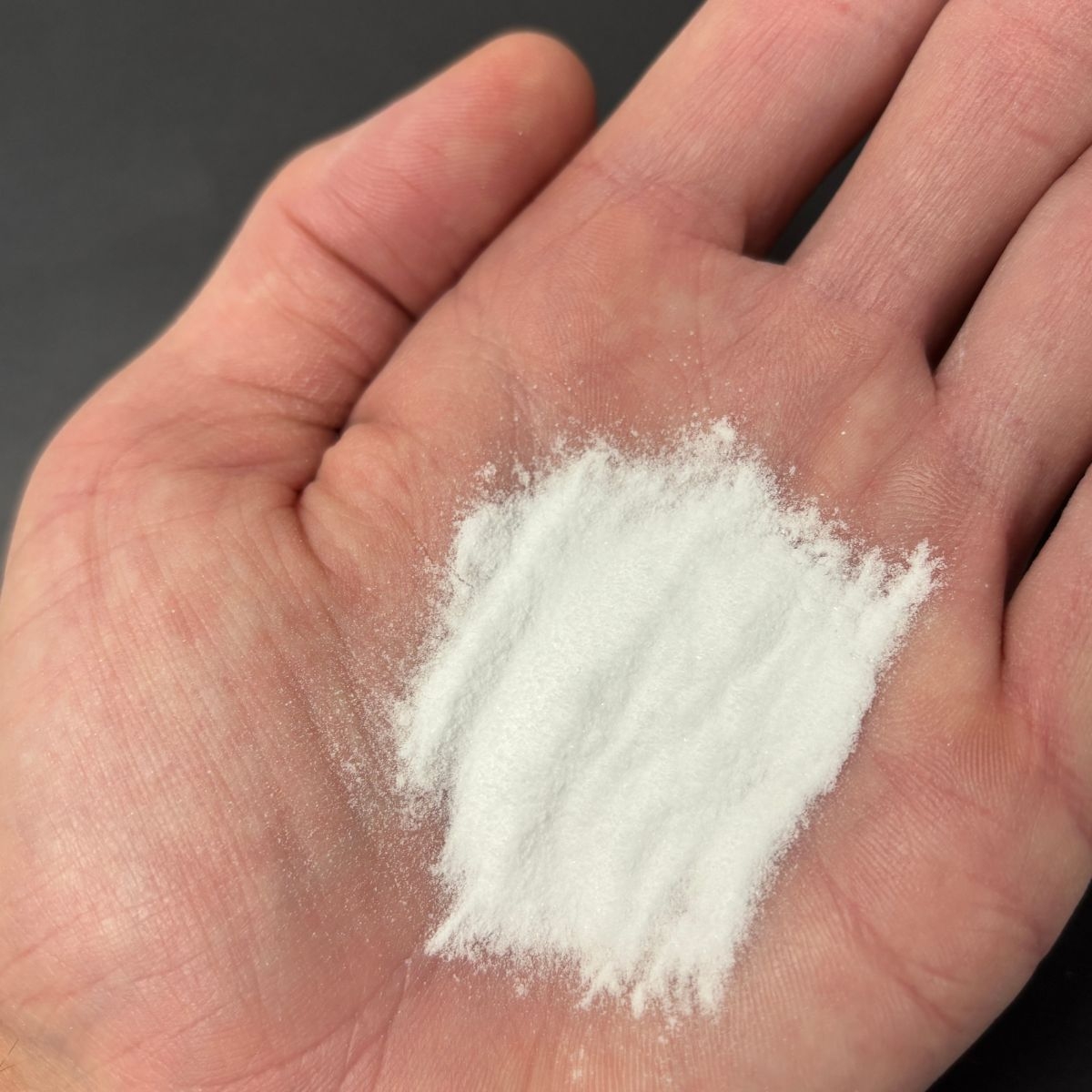 Weisses Natronpulver in einer Hand auf schwarzem Hintergrund