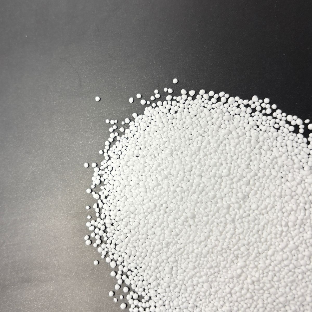 Weisses Kaliumcarbonat-Granulat auf dunklem Hintergrund verteilt