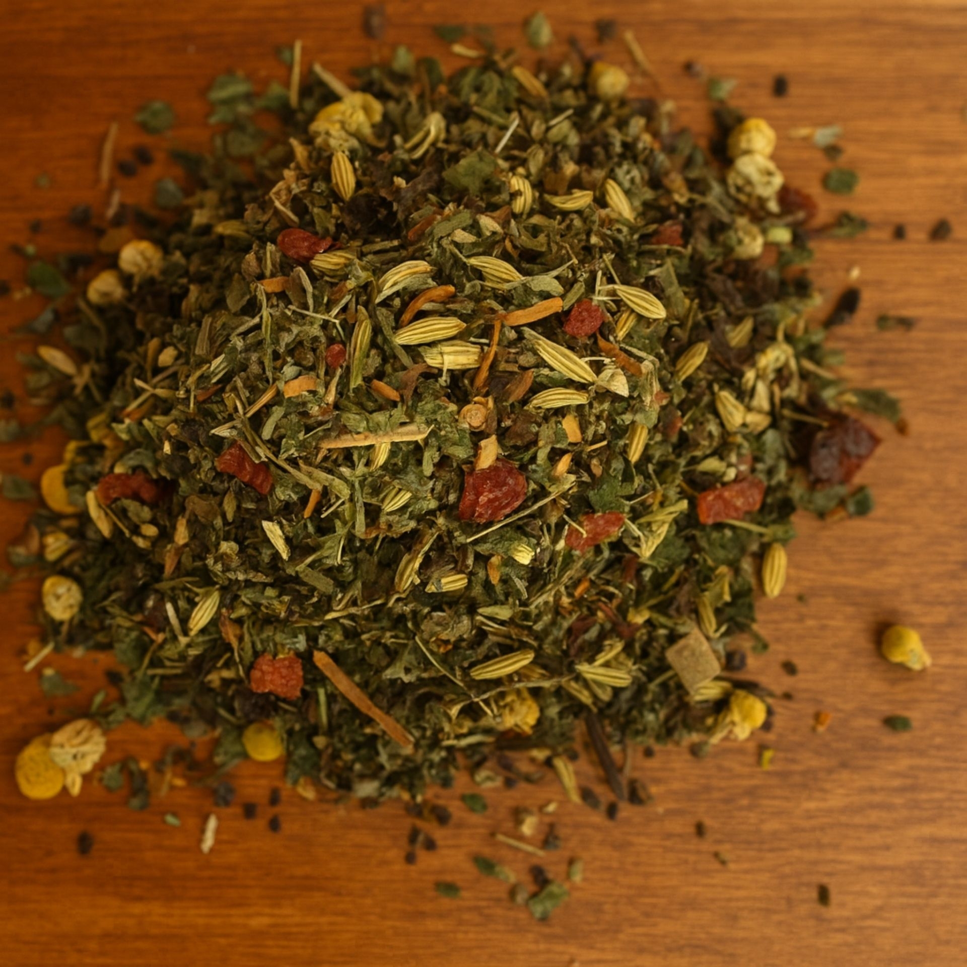 Lose Kraeutermischung „Wohlfuehltee“ mit Blueten und Fruechten auf einem Holztisch verstreut
