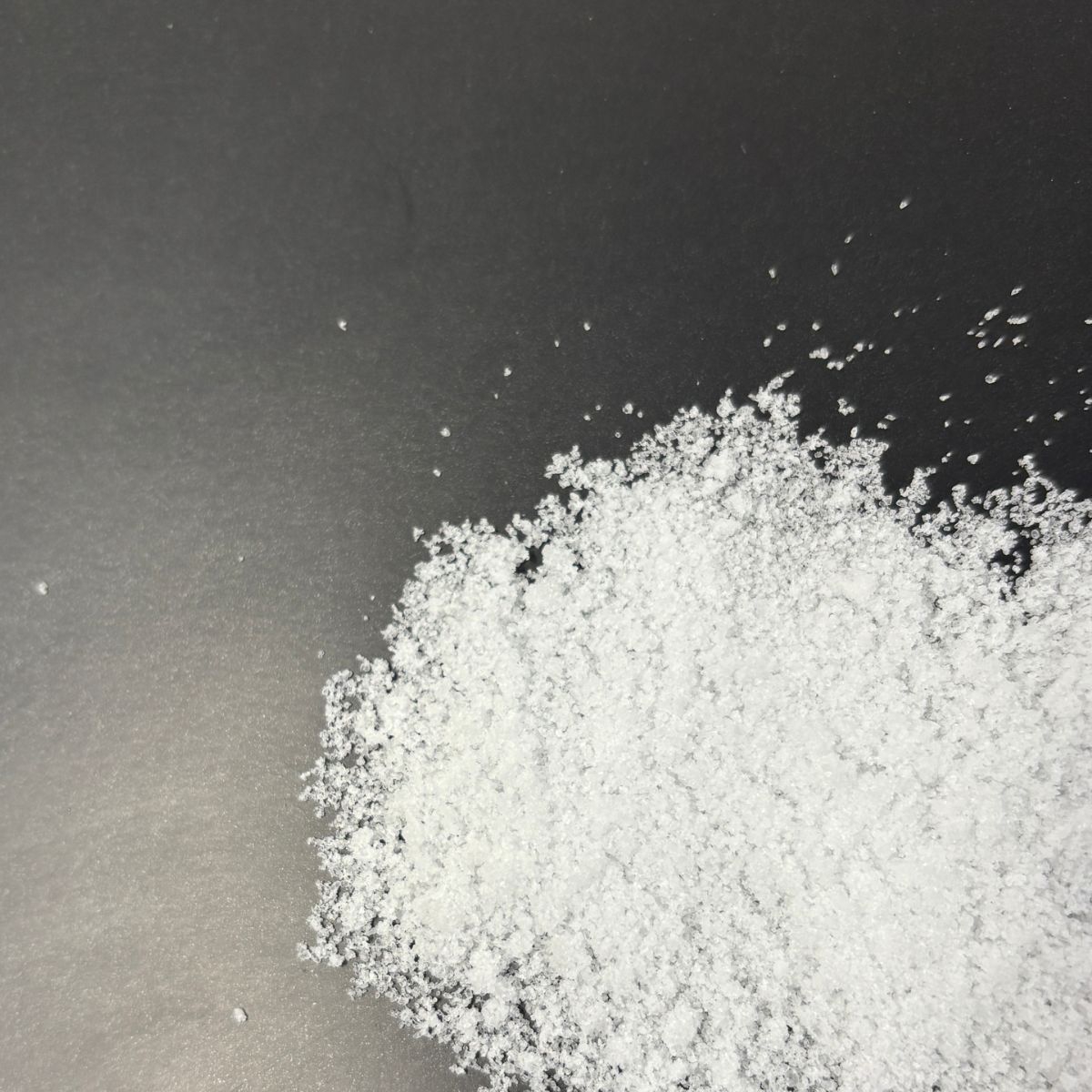 Nahaufnahme von weissem Magnesiumchlorid-Pulver auf schwarzem Hintergrund